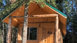 A wooden cabin with a green roof, a window, and a door with a 'Welcome' sign. - CAM'S LAKESIDE BUNKHOUSE  (Soldotna)