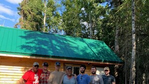 A group of people standing in front of a cabin with a green roof, surrounded by trees. - CAM'S LAKESIDE BUNKHOUSE  (Soldotna)