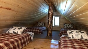 A cozy attic bedroom with wooden walls and sloped ceilings, featuring two beds with plaid bedding and moose-themed pillows. - CAM'S LAKESIDE BUNKHOUSE  (Soldotna)
