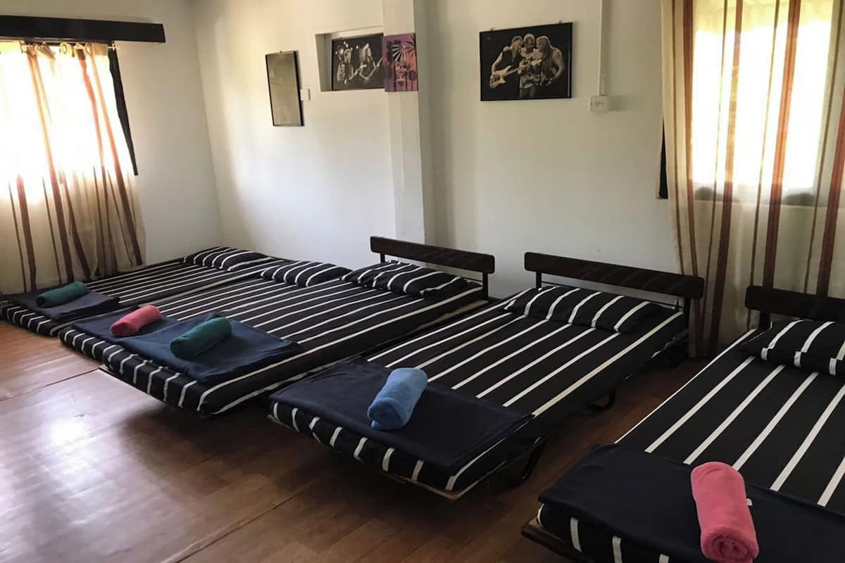 A room with four single beds, each with a black and white striped mattress and matching pillows. There are curtains on the windows, and wall art is visible.