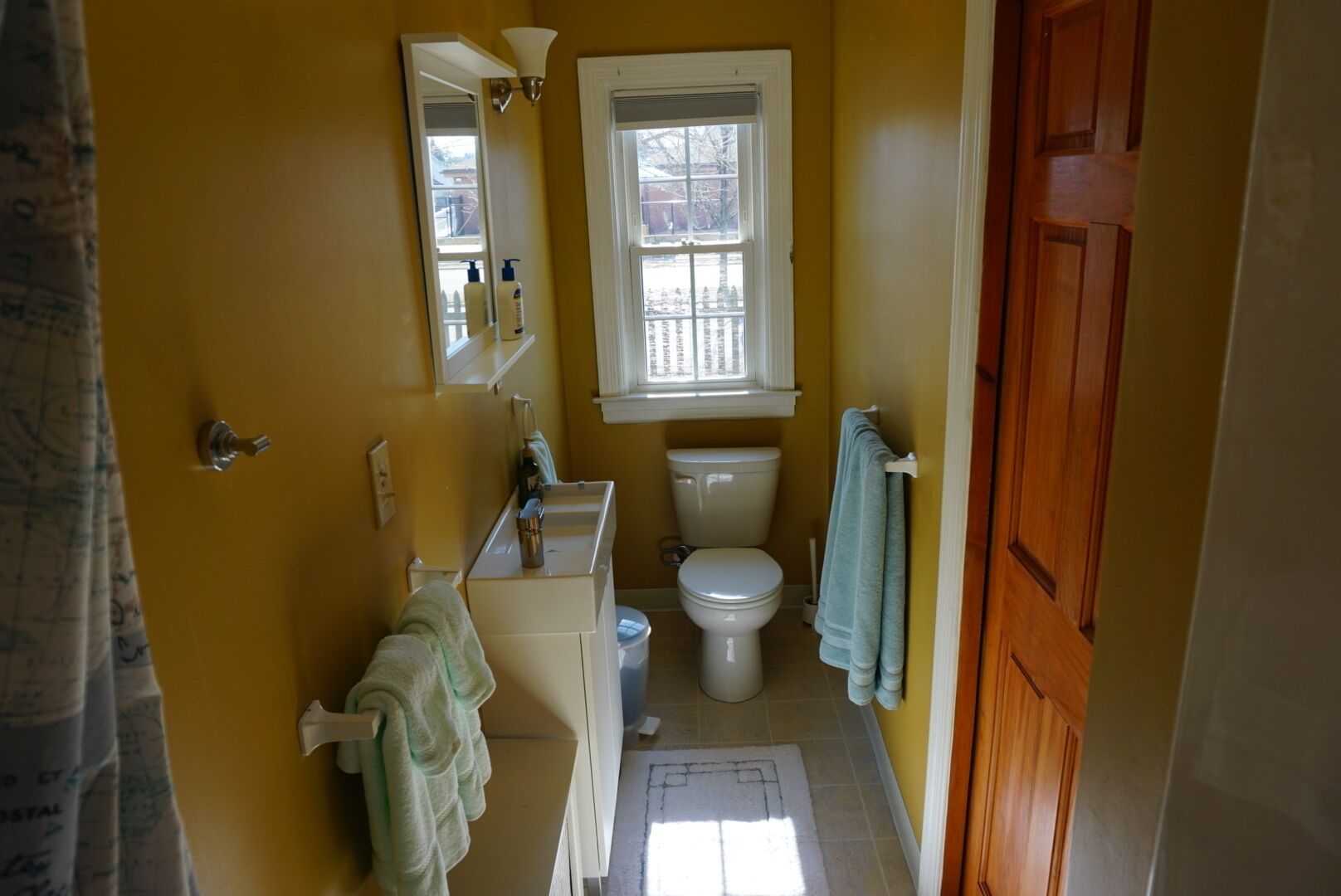 Kylpyhuoneessa on wc, pesuallas ja peili. WC:n yläpuolella on ikkuna ja seinällä pyyheteline, jossa on pyyhkeitä.