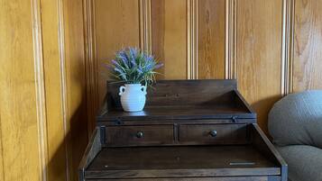 A wooden side table with a white vase containing lavender flowers, placed against a wooden paneled wall.