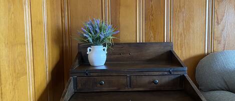 A wooden side table with a white vase containing lavender flowers, placed against a wooden paneled wall.