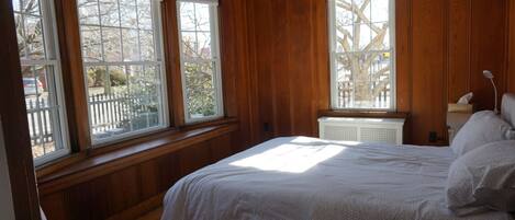 A bedroom with a large bed, wooden walls, and three windows.