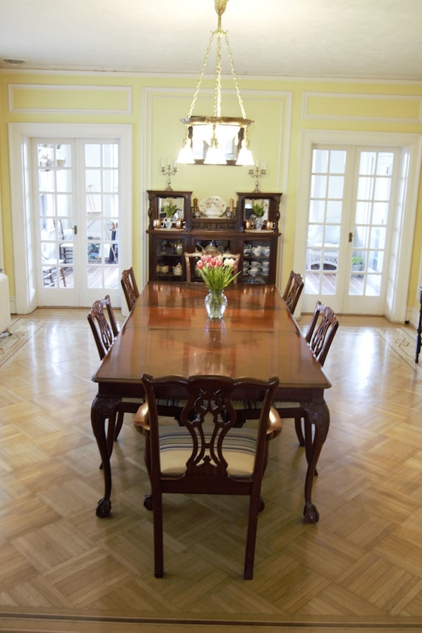 A dining room with a long wooden table surrounded by chairs, a chandelier, and a vase with flowers.