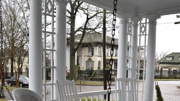 Eine Veranda mit weißen Korbmöbeln, darunter eine Schaukel und Stühle, unter einer weißen Markise mit Säulen.