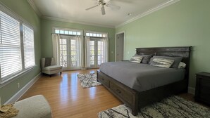 A bedroom with a bed, a nightstand, a dresser, a chair, a ceiling fan, and a window with blinds.
