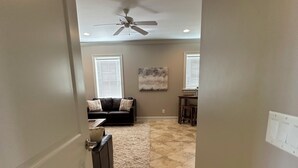 A hallway with a ceiling fan, a dark-colored sofa with pillows, a small table, and a rug.