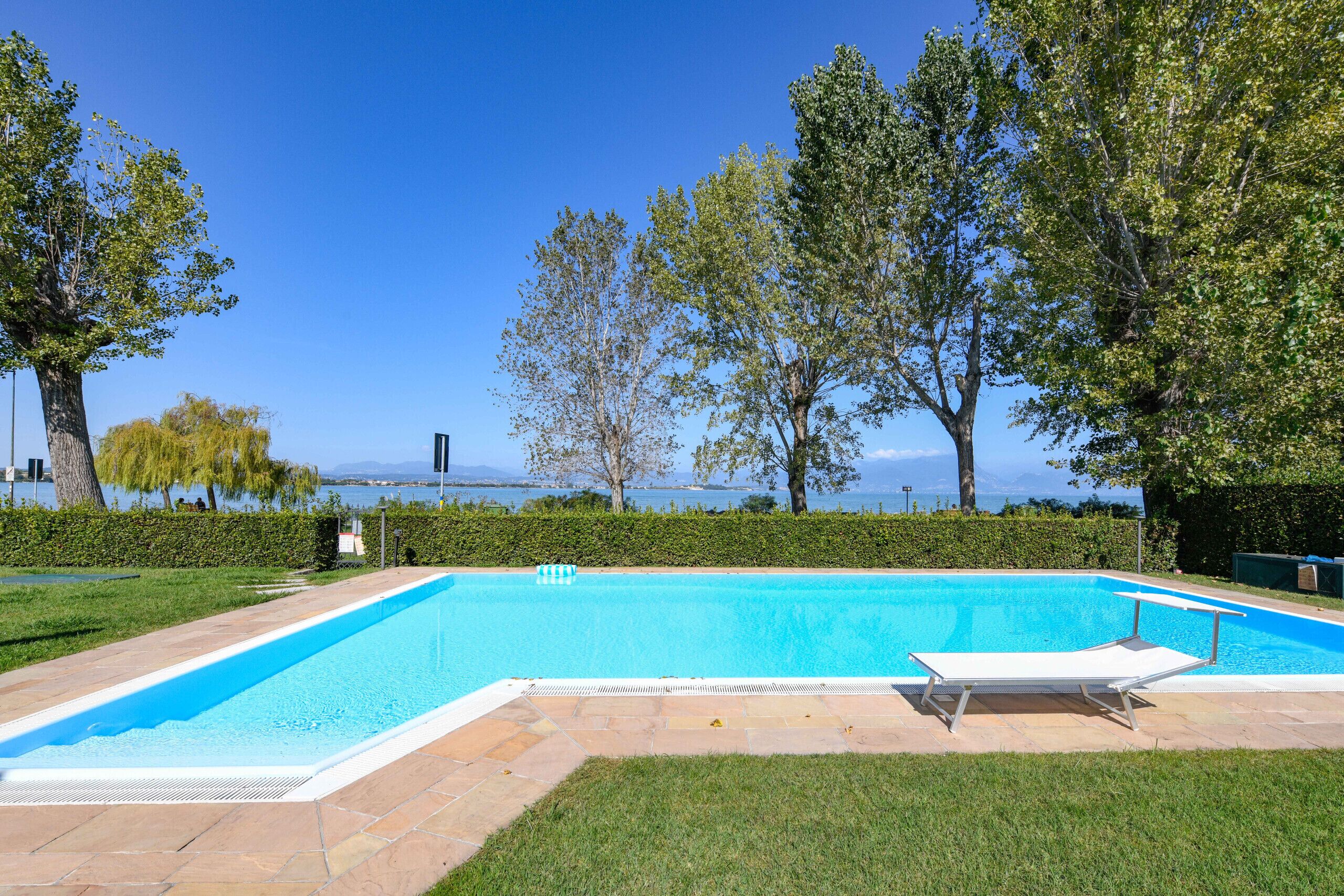A rectangular swimming pool with a clear blue water, surrounded by a stone deck and a grassy area.