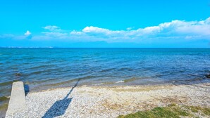 A clear view of a beach with calm water and a concrete walkway leading to the shore. - My Lakeside Dream (Sirmione)
