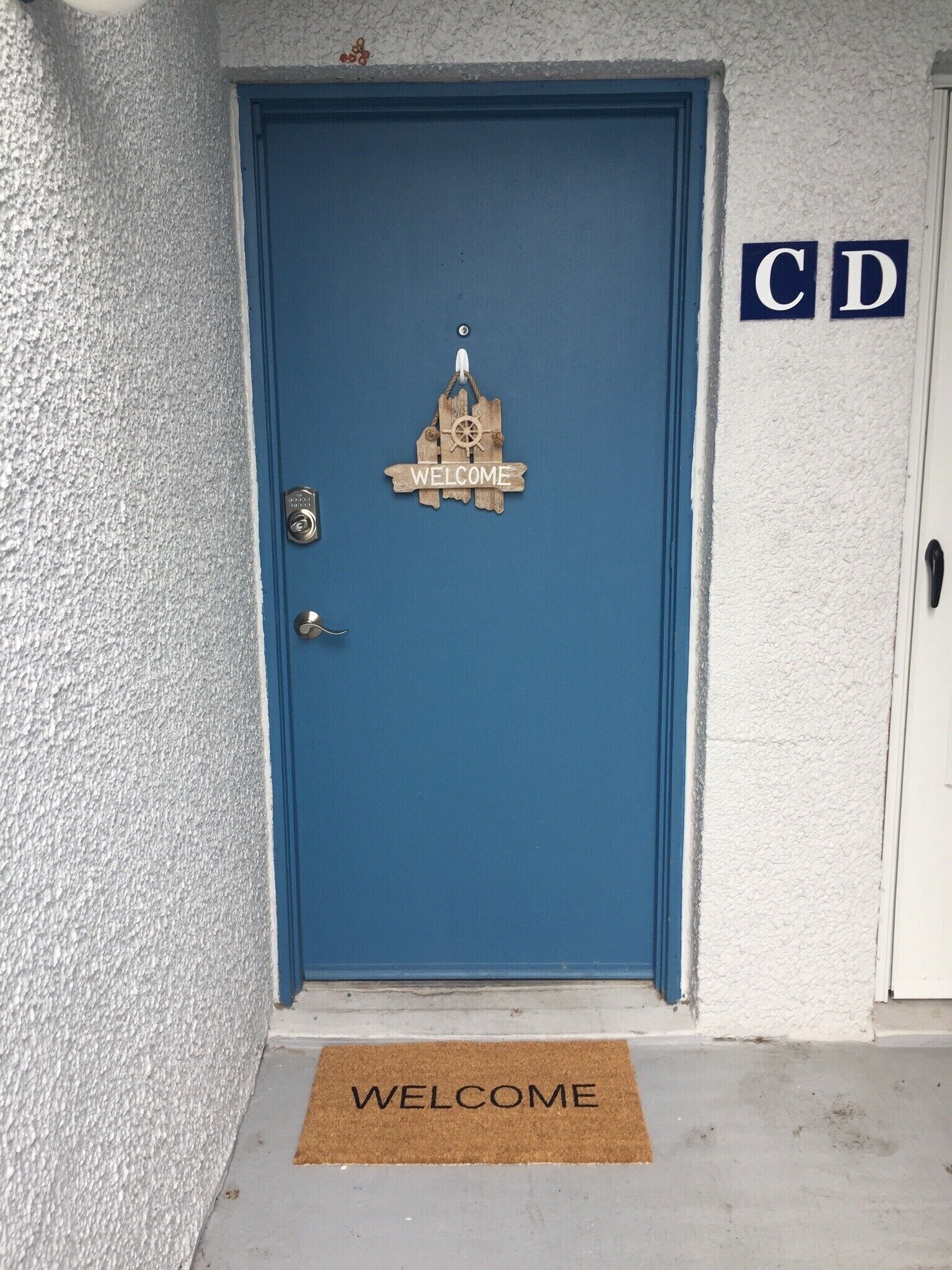 A blue door with a 'WELCOME' sign and a doormat.
