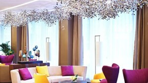 En moderne hotellobby med en beige sofa, gule og lilla lænestole og et rundt sofabord.