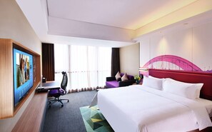Quarto de hotel com uma cama grande, uma escrivaninha com cadeira, televisão na parede e janela com cortinas.