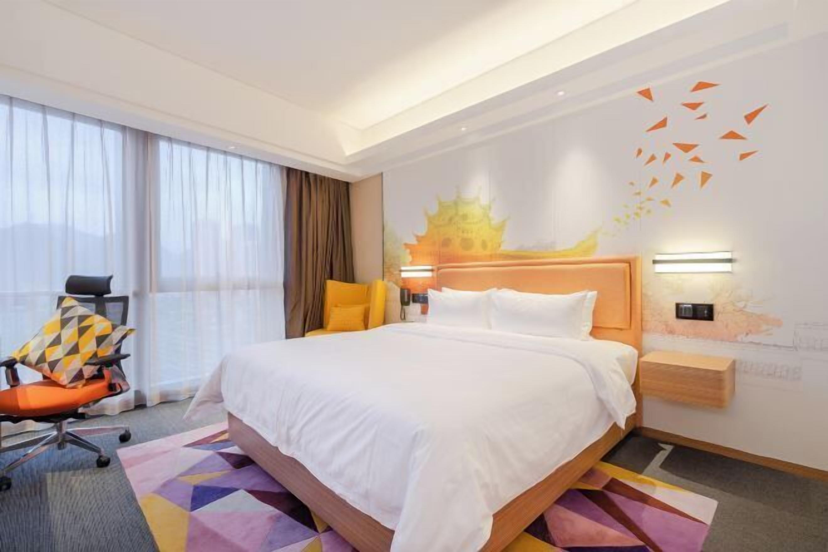 A hotel room with a large bed, a chair, a desk, and a wall with a decorative mural.