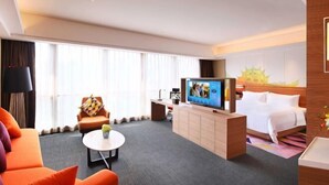 Et hotelværelse med seng, fjernsyn, sofa, sofabord og skrivebord.