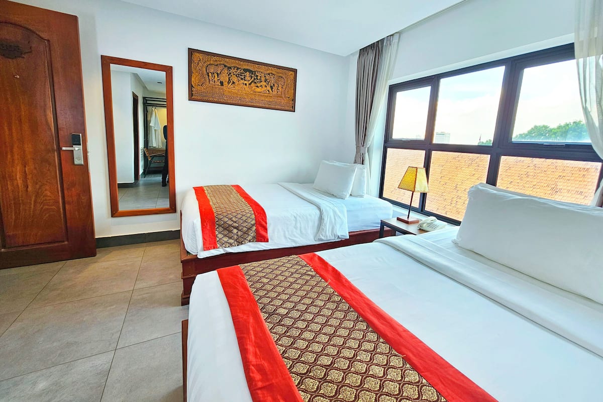 Quarto de hotel com duas camas, uma janela grande com cortinas, um abajur e uma obra de arte na parede.