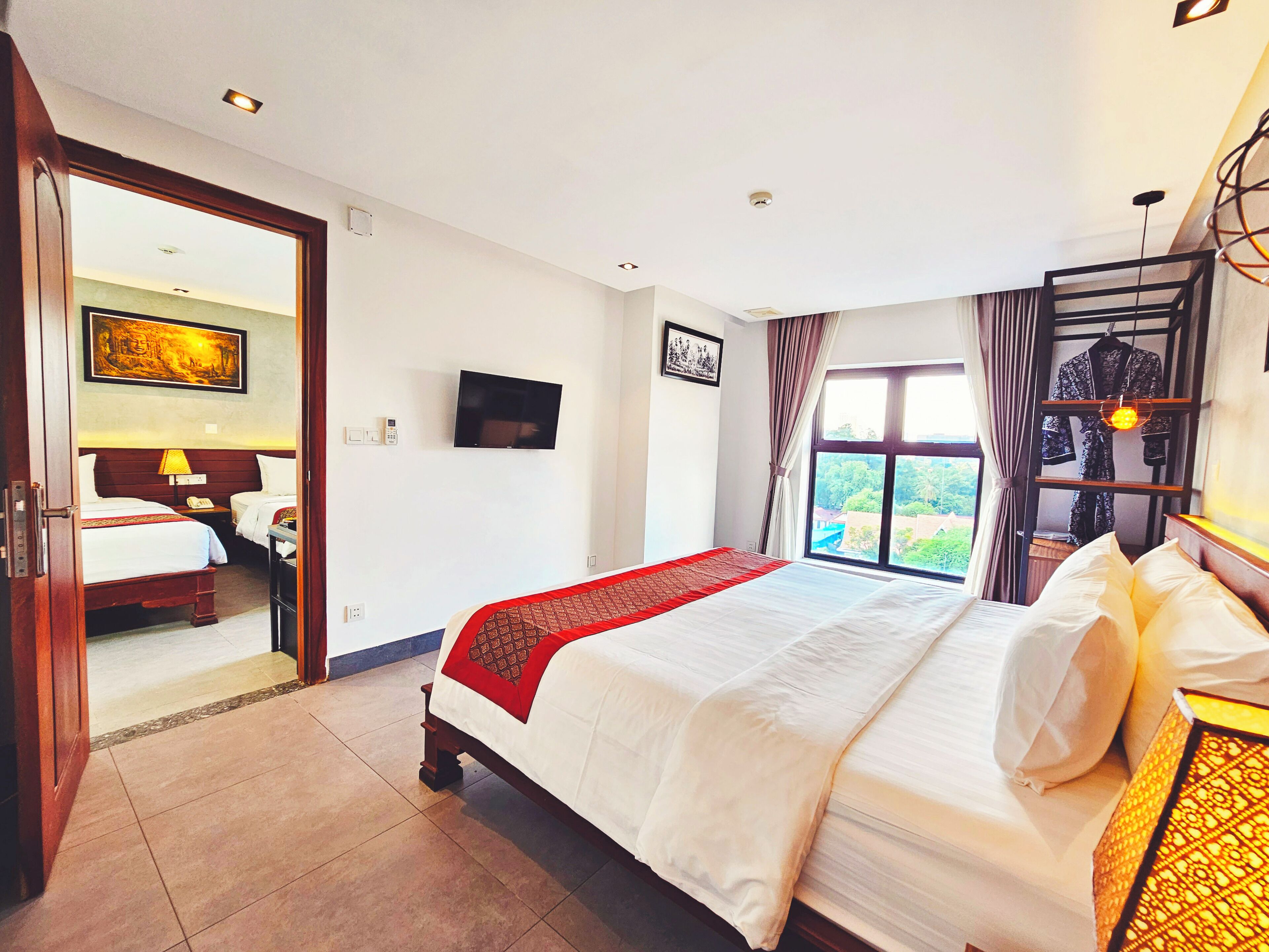 A hotel room with a large bed, a TV, a wardrobe, and a window with a view.