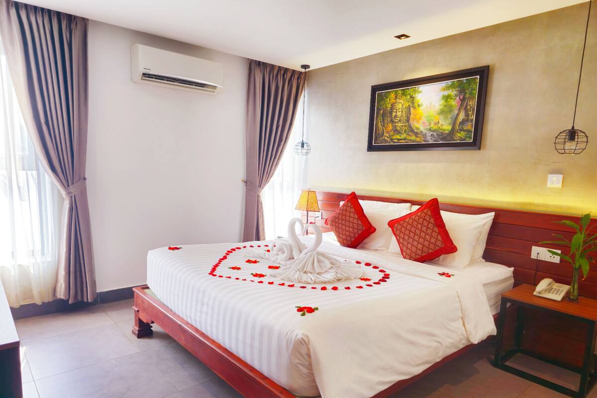 Quarto de hotel com uma cama grande, mesa de cabeceira com telefone, ar condicionado fixado na parede e um quadro sobre a cama.