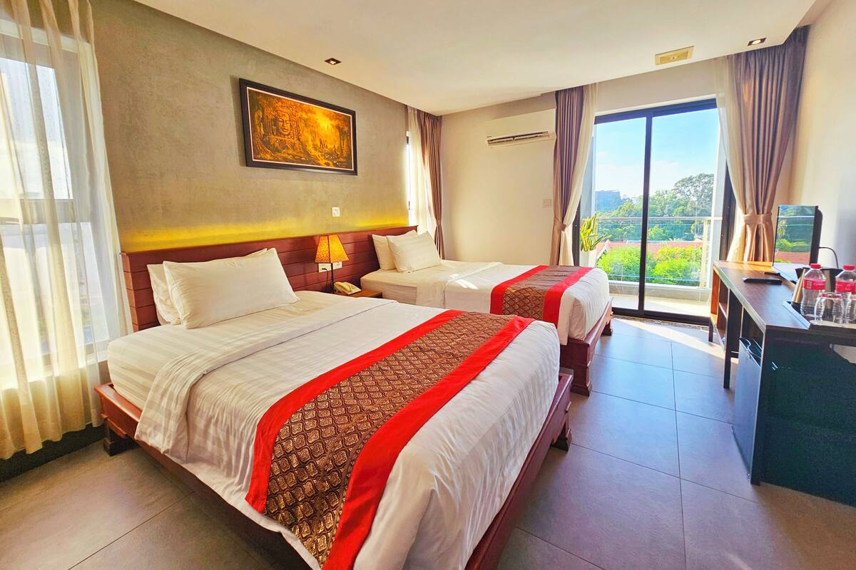 Quarto de hotel com duas camas, uma escrivaninha, televisão e uma janela grande com vista.