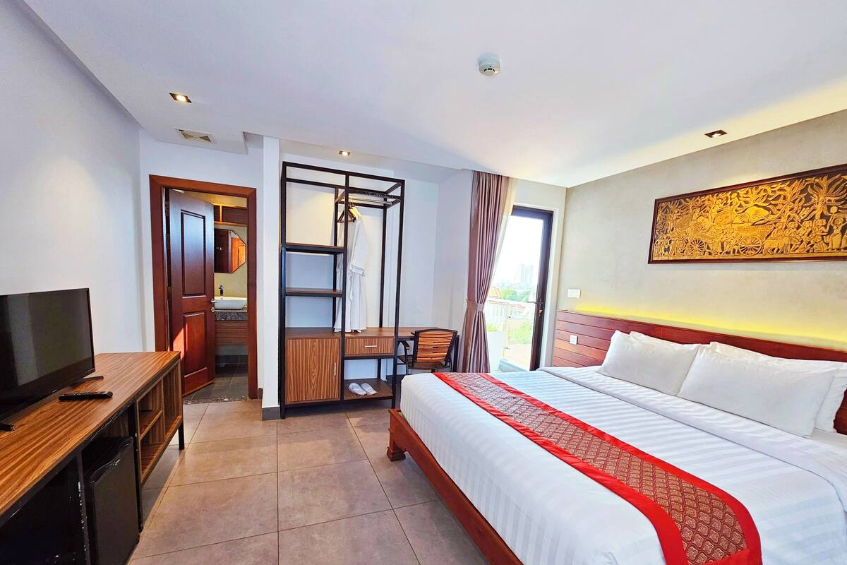 Quarto de hotel com cama, televisão, escrivaninha e banheiro.