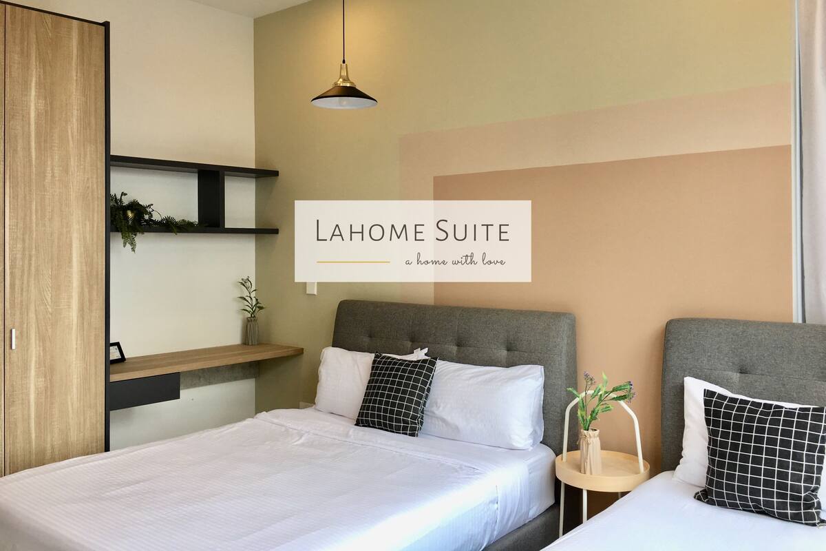 A modern hotel room with a bed, bedside tables, a hanging light fixture, and a wall-mounted shelf with plants.
