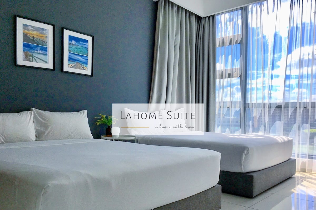 A modern hotel room with a large bed, a smaller bed, a nightstand, and a window with curtains. There are two framed pictures on the wall.