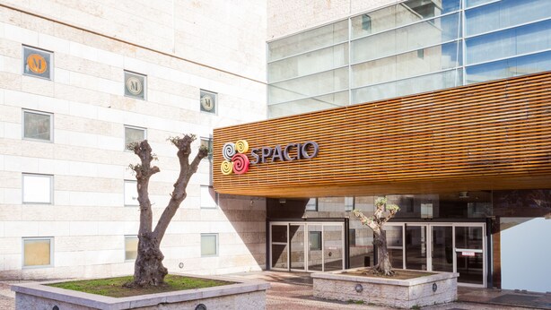 A modern building with a wooden facade and a sign reading "SPACIO". There are two trees in planters in front of the entrance. - Stupendo Airport Studio 1 (Lisboa)