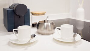 A modern kitchen with two white cups on saucers, a stainless steel teapot, a dark blue appliance, and a clear glass container. - Stupendo Airport Studio 1 (Lisboa)