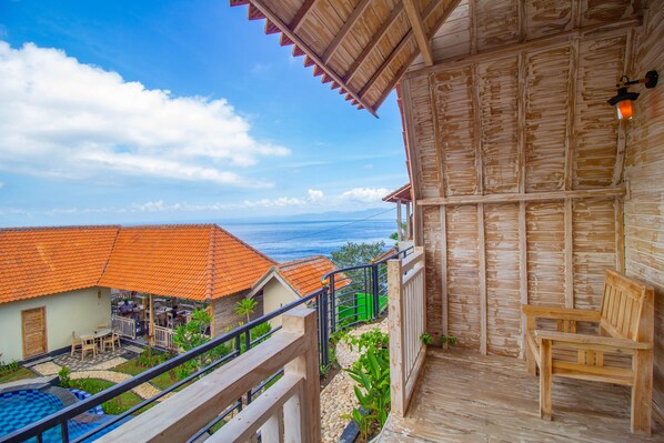 Un balcón de madera con un banco, una piscina y vistas al océano y otros edificios.