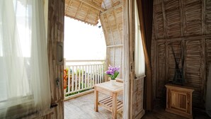 A wooden room with a balcony, a small table with a vase of flowers, and a cabinet. - Unicorn Bungalow (Penida Island)