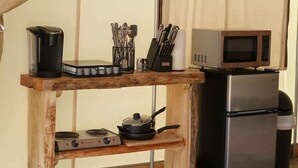 Een kleine keukenhoek met een koffiezetapparaat, magnetron, fornuis en keukengerei op een houten plank.