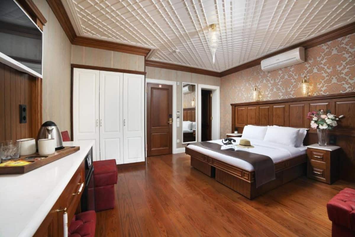 A bedroom with a wooden bed, a desk with a chair, a wardrobe, and a ceiling with a grid pattern.