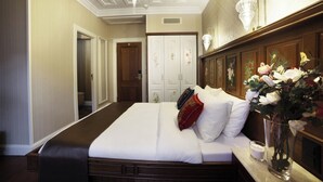 Camera d'albergo con un letto grande, un comodino con un vaso di fiori, una testiera in legno e un armadio decorato con motivi floreali.