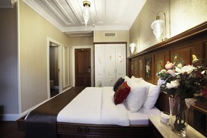 A hotel room with a large bed, a bedside table with a vase of flowers, a wooden headboard, and a wardrobe with floral decorations.