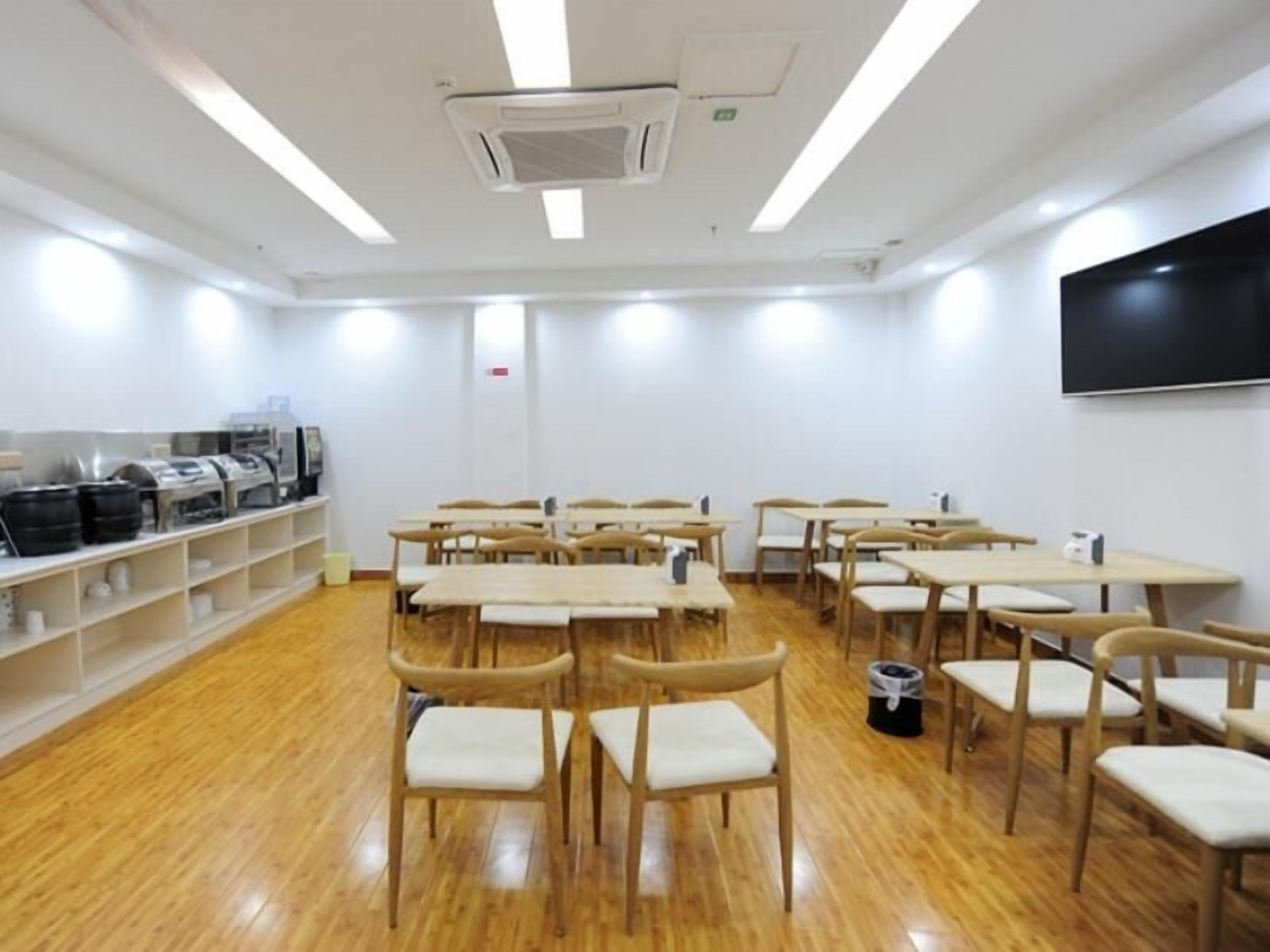 Une salle de classe avec des pupitres et des chaises en bois, un tableau blanc et un téléviseur fixé au mur.