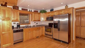 Una cocina con armarios de madera, electrodomésticos de acero inoxidable, lavavajillas, microondas y refrigerador.