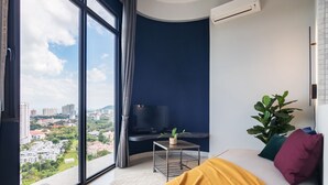 A modern living room with a large window, a flat-screen TV, a small side table, and a sofa with cushions. - Arte S Family Suites (George Town)