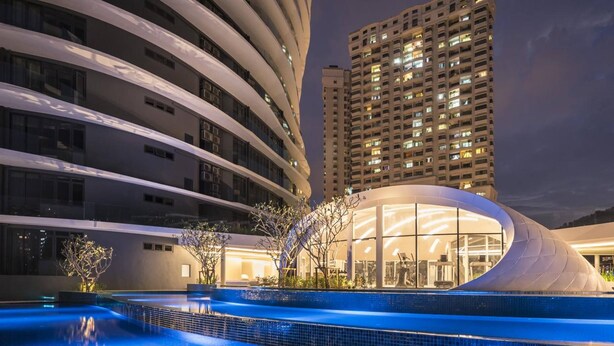 A modern hotel with a curved exterior, a swimming pool, and a view of surrounding high-rise buildings. - Arte S Family Suites (George Town)