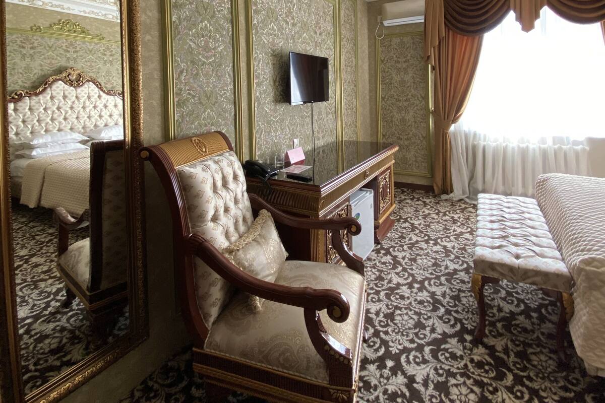 Une chambre luxueuse dotée d’un grand miroir, de meubles richement décorés, d’un téléviseur et d’un tapis à motifs.