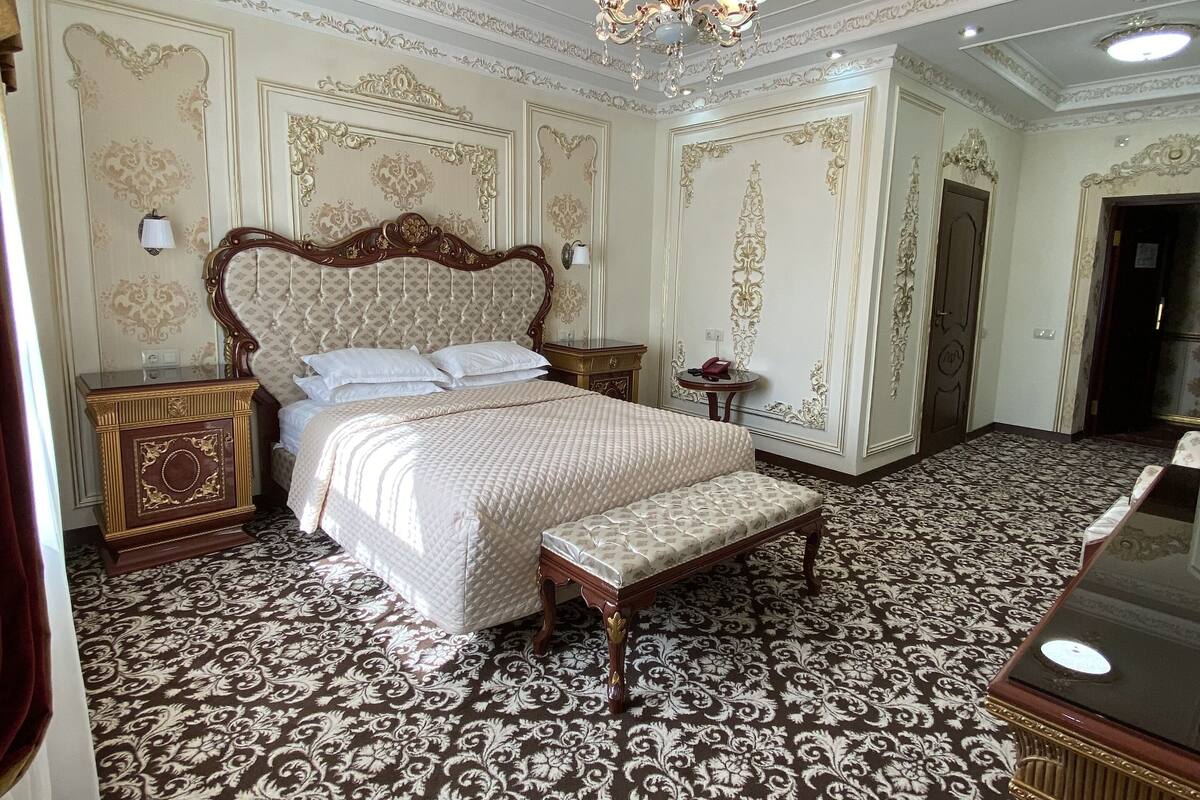 Une chambre spacieuse avec un grand lit, un banc et un lustre.
