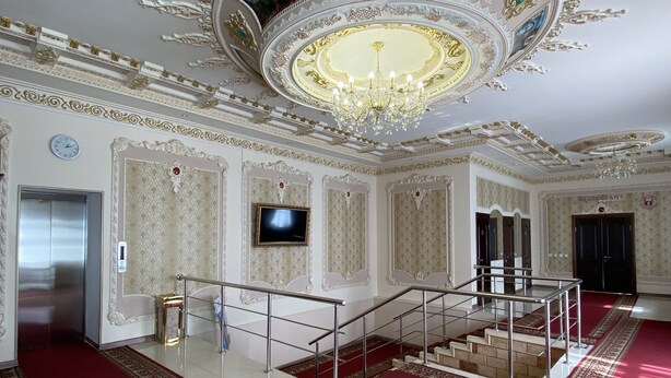Une vaste pièce dotée de décorations élaborées au plafond, d’un lustre et d’un sol recouvert d’un tapis rouge.
