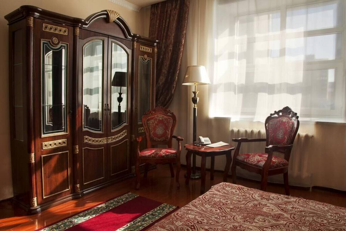 Une pièce comprenant un grand meuble en bois, deux chaises, une petite table et un lit recouvert d’une couvre-lit à motifs.