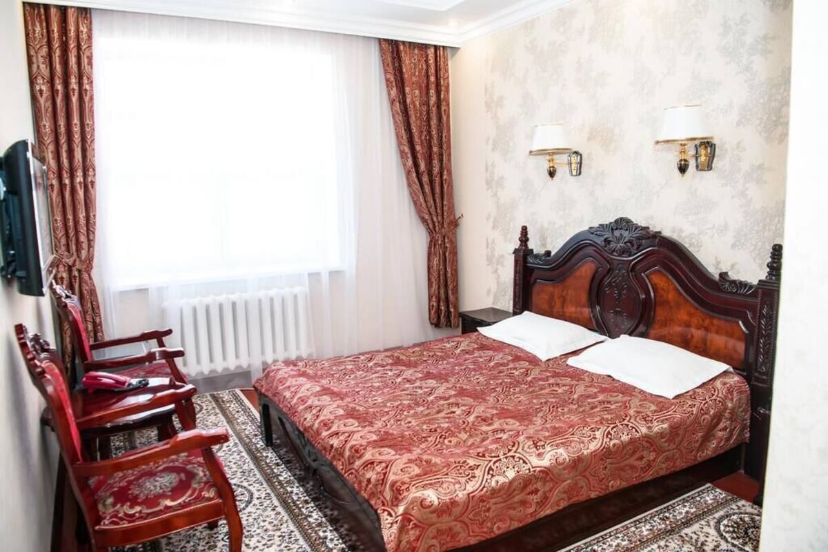 Une chambre à coucher avec un grand lit, deux lampes de chevet, un radiateur et une fenêtre avec des rideaux.