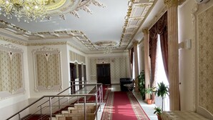 Un vaste hall d’entrée avec un tapis rouge, un plafond richement décoré et un escalier menant à une salle à manger.