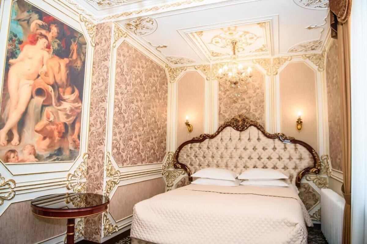 Une chambre à coucher luxueuse, avec un lit somptueux, un grand tableau au mur et un plafond décoratif.