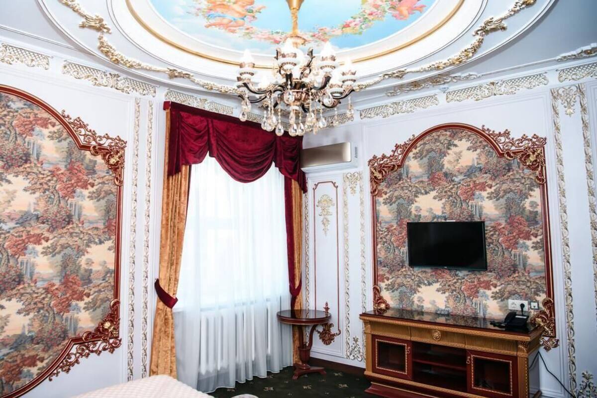Une chambre luxueuse, dotée d’une décoration raffinée, d’un lustre, d’un grand miroir et d’un téléviseur posé sur un meuble en bois.