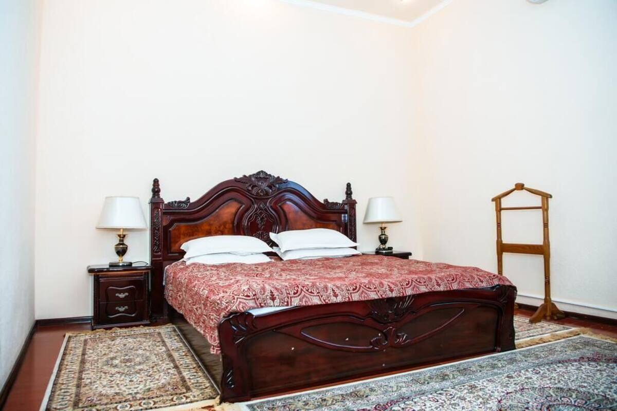 Une chambre avec un lit en bois, deux tables de chevet avec des lampes, un fauteuil suspendu et un tapis à motifs.