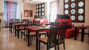 Un restaurant dont le mobilier est rouge et noir, avec des tables, des chaises et un canapé rouge.