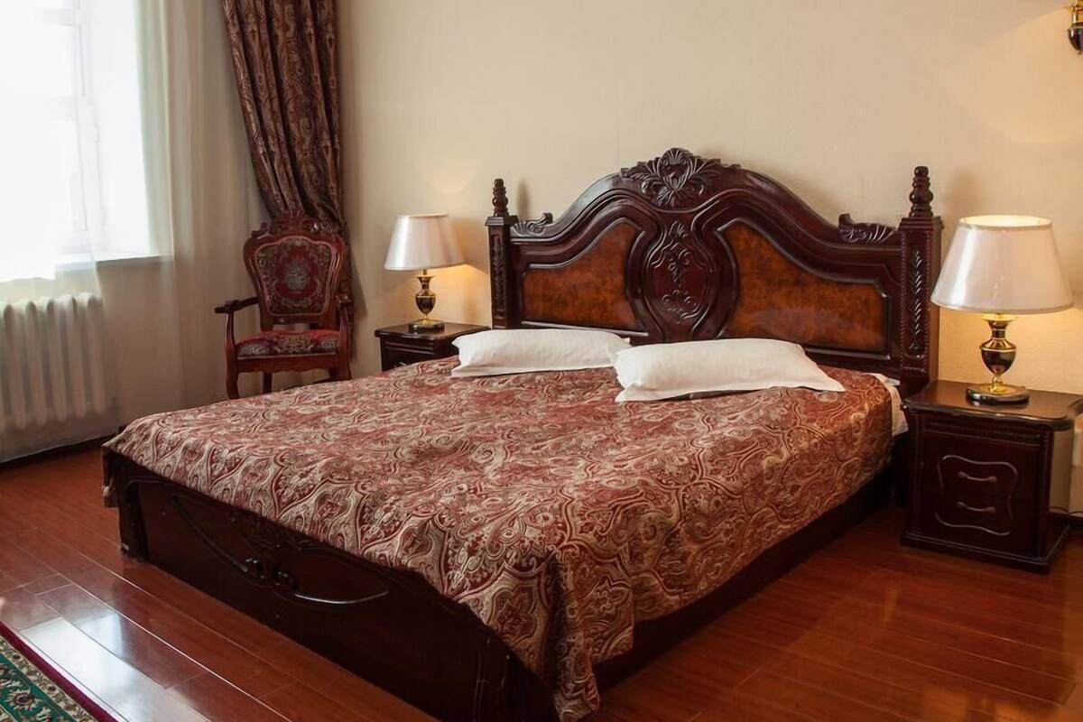 Un grand lit avec une couvre-lit à motifs, deux tables de chevet avec des lampes, une chaise et un radiateur.
