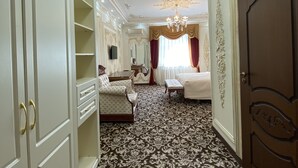 Une chambre d’hôtel avec un tapis à motifs, un lustre, un lit, un bureau et une armoire.